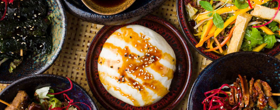 A vibrant spread of vegan Vietnamese dishes — steamed bao, fresh salads and skewers on a woven mat
