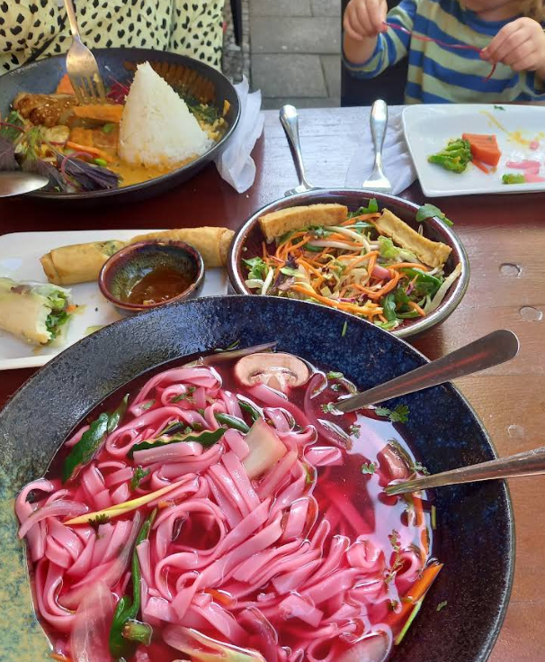 Bowl of pho with bright pink rice noodles and herbs